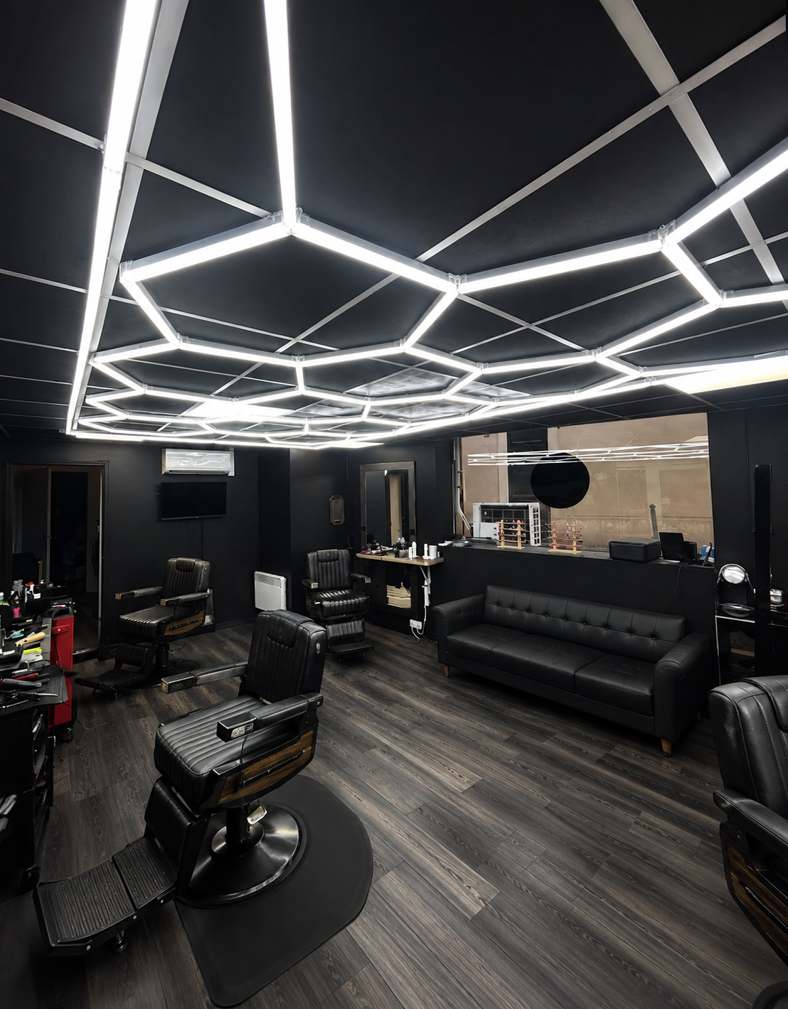 Intérieur du salon Maison Barbier avec plafond lumineux hexagonal et fauteuils noirs
